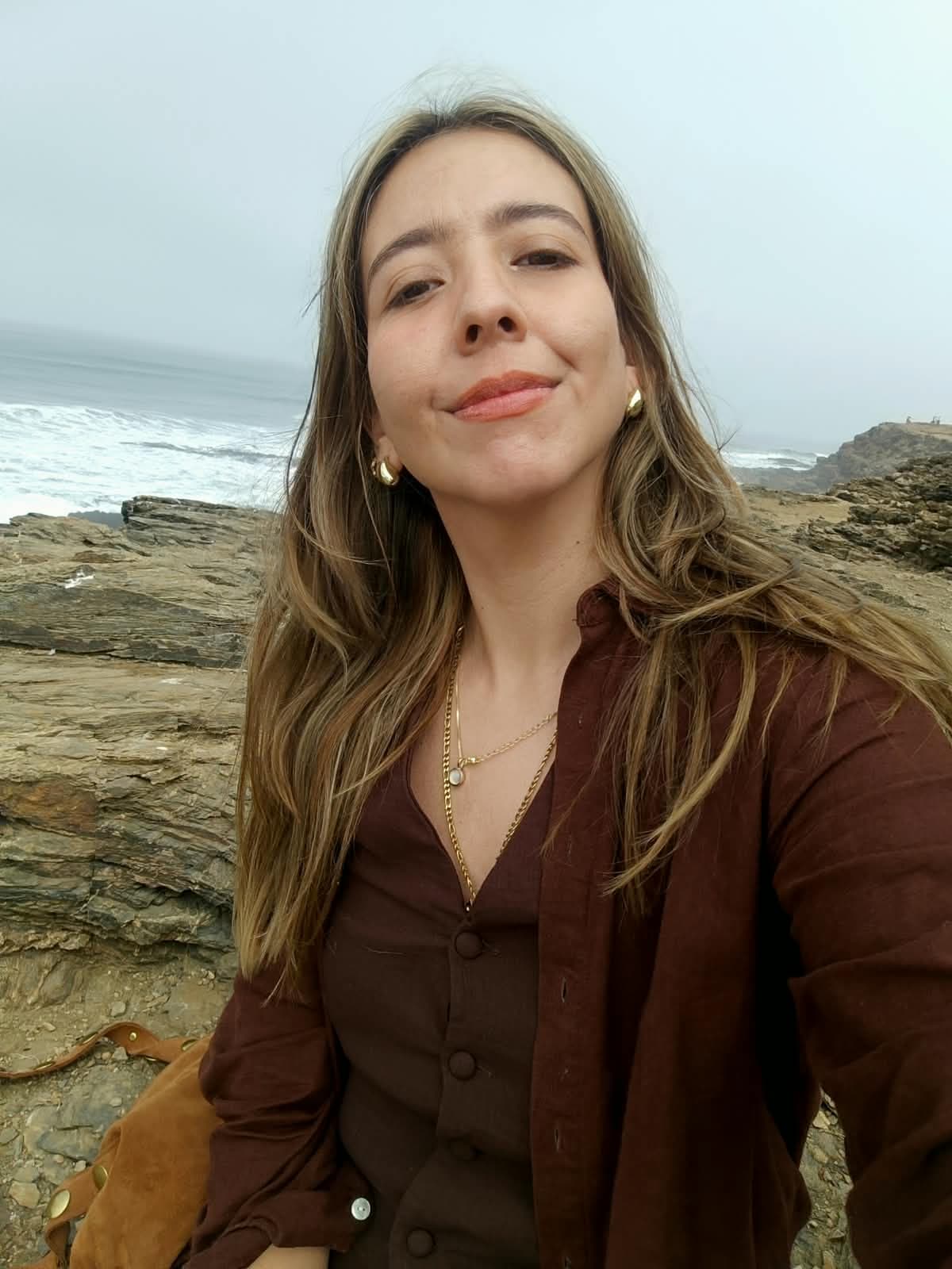 Pía Poblete sonriendo frente al mar, sobre las rocas de la costa
